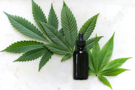Three green marijuana leaves appear on a white background; a small black tincture bottle sits in the foreground